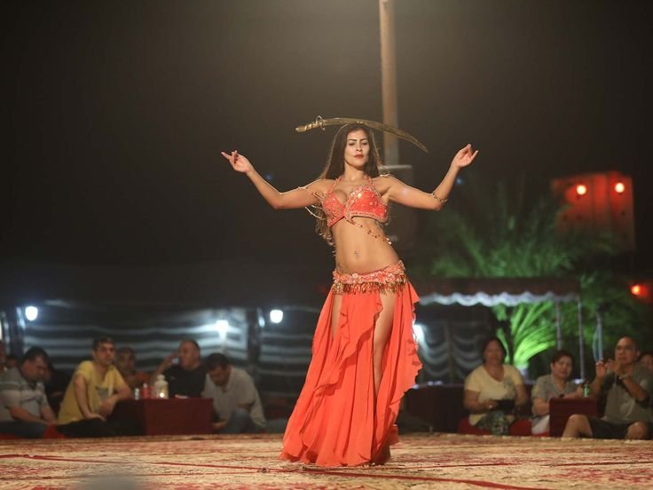 Belly dancer in orange costume performing at the desert safari camp