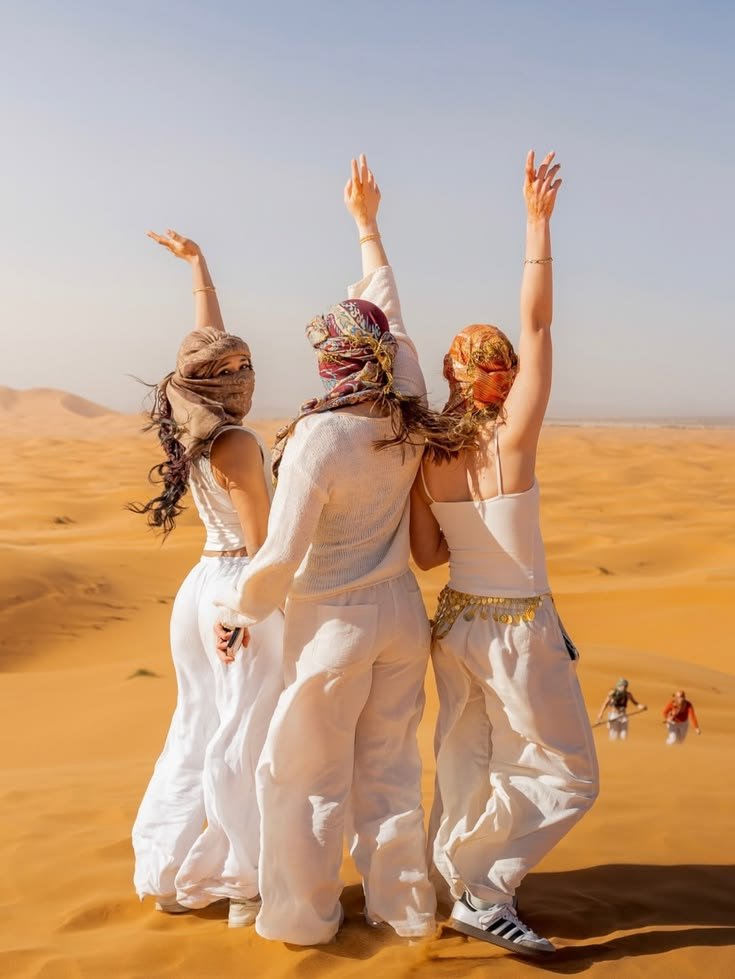 Group of friends raising their arms on the desert dunes
