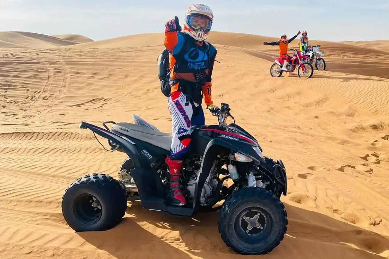 Rider posing on a quad bike with motocross bikes on the sand dunes