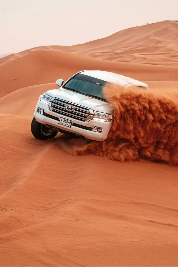 Silver Toyota Land Cruiser turning on a red desert dune
