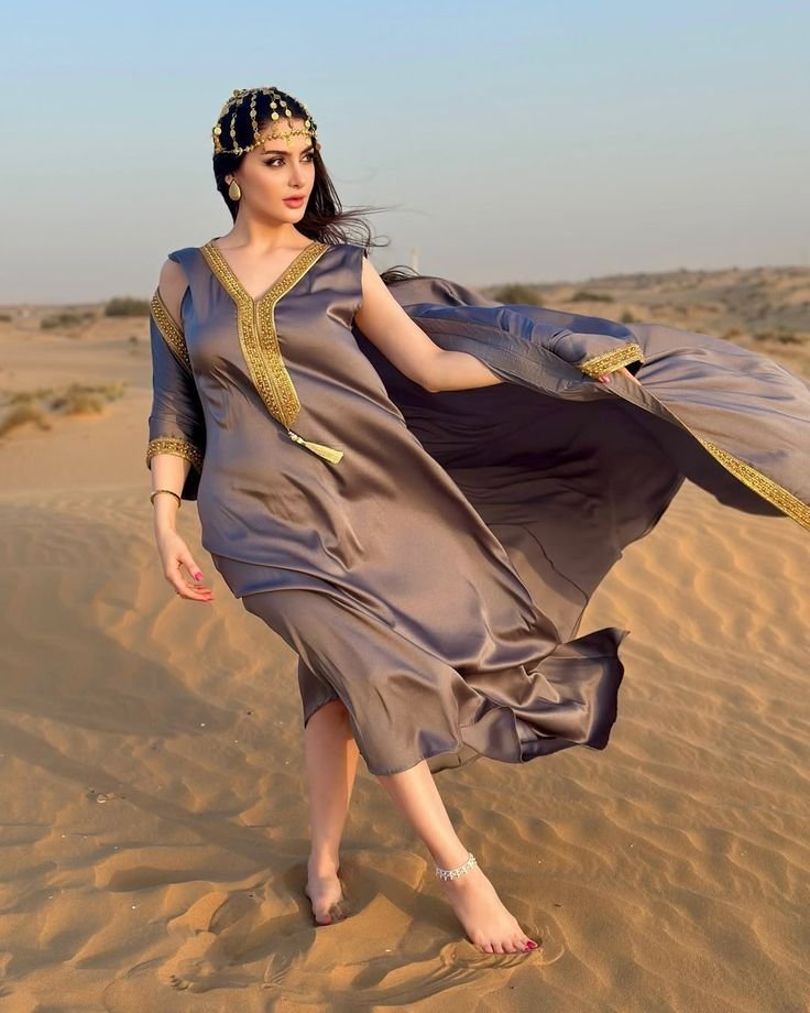 Woman in a flowing Arabic gown walking on the desert dunes